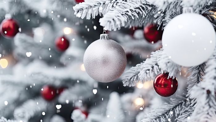 Bild mit schneebedecktem Tannenbaum an dem Weihnachtskugeln hängen